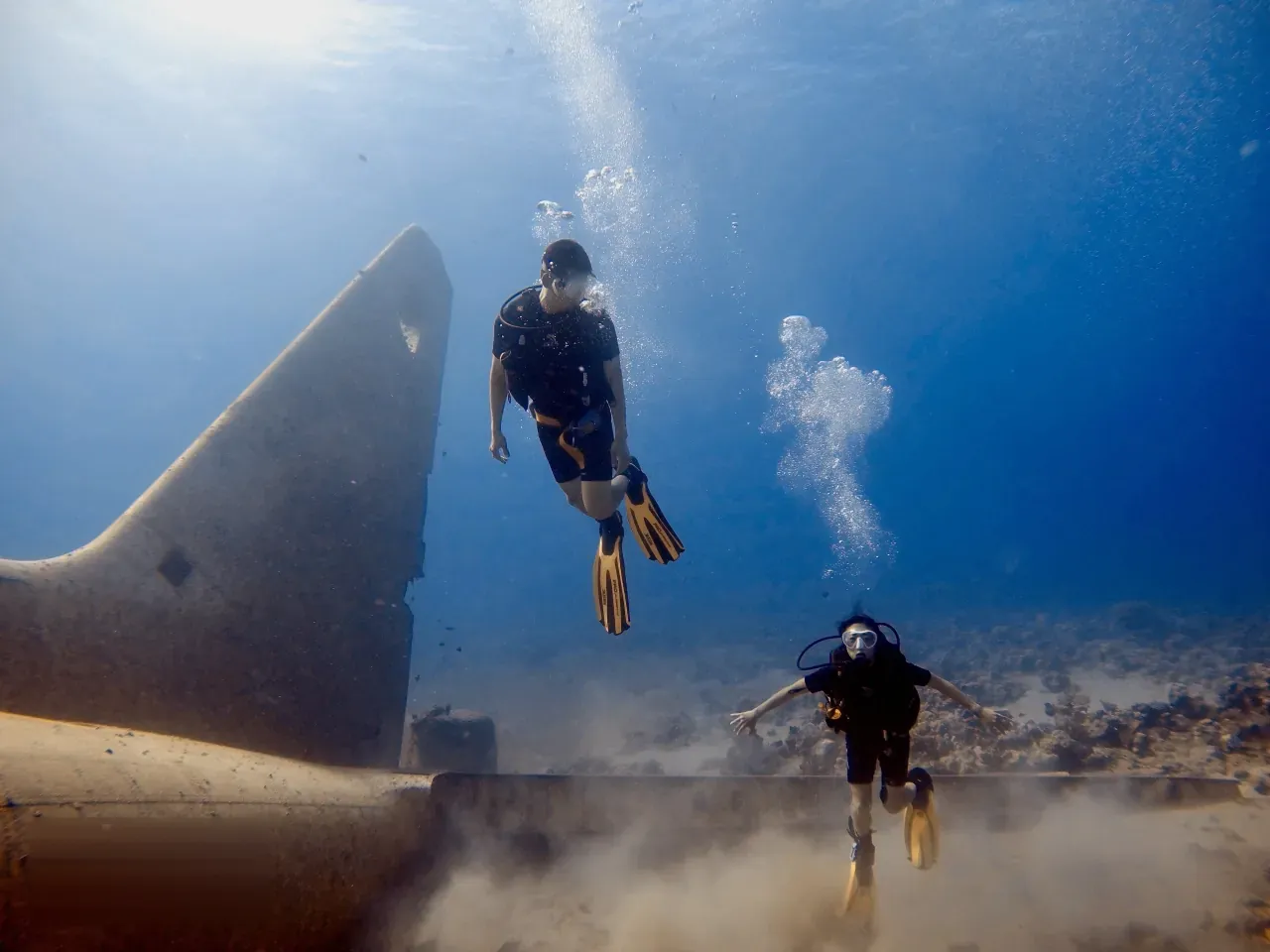 Two scuba divers swimming above a large sunken wreck in the blue water of the Red Sea off Aqaba, Jordan.
