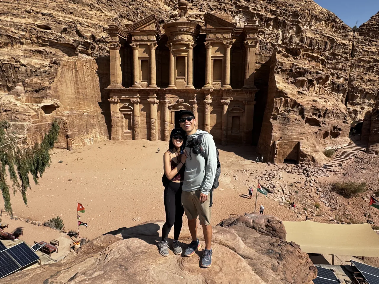 Deyu and Meesh standing in front of the tall columned facade of the Monastery carved into the rock at Petra, Jordan.